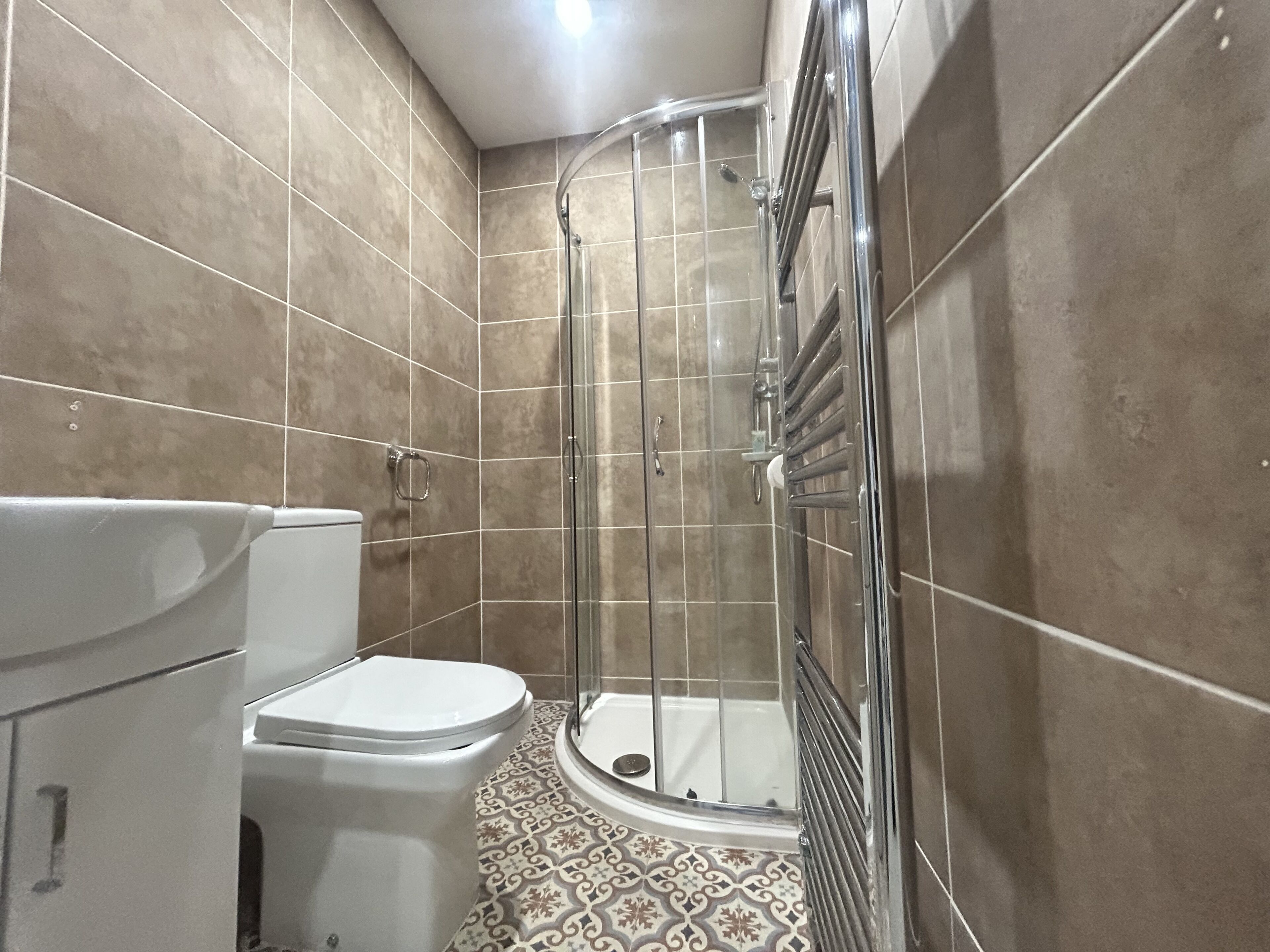 A bathroom with a toilet, a shower with a glass door, and patterned floor tiles.