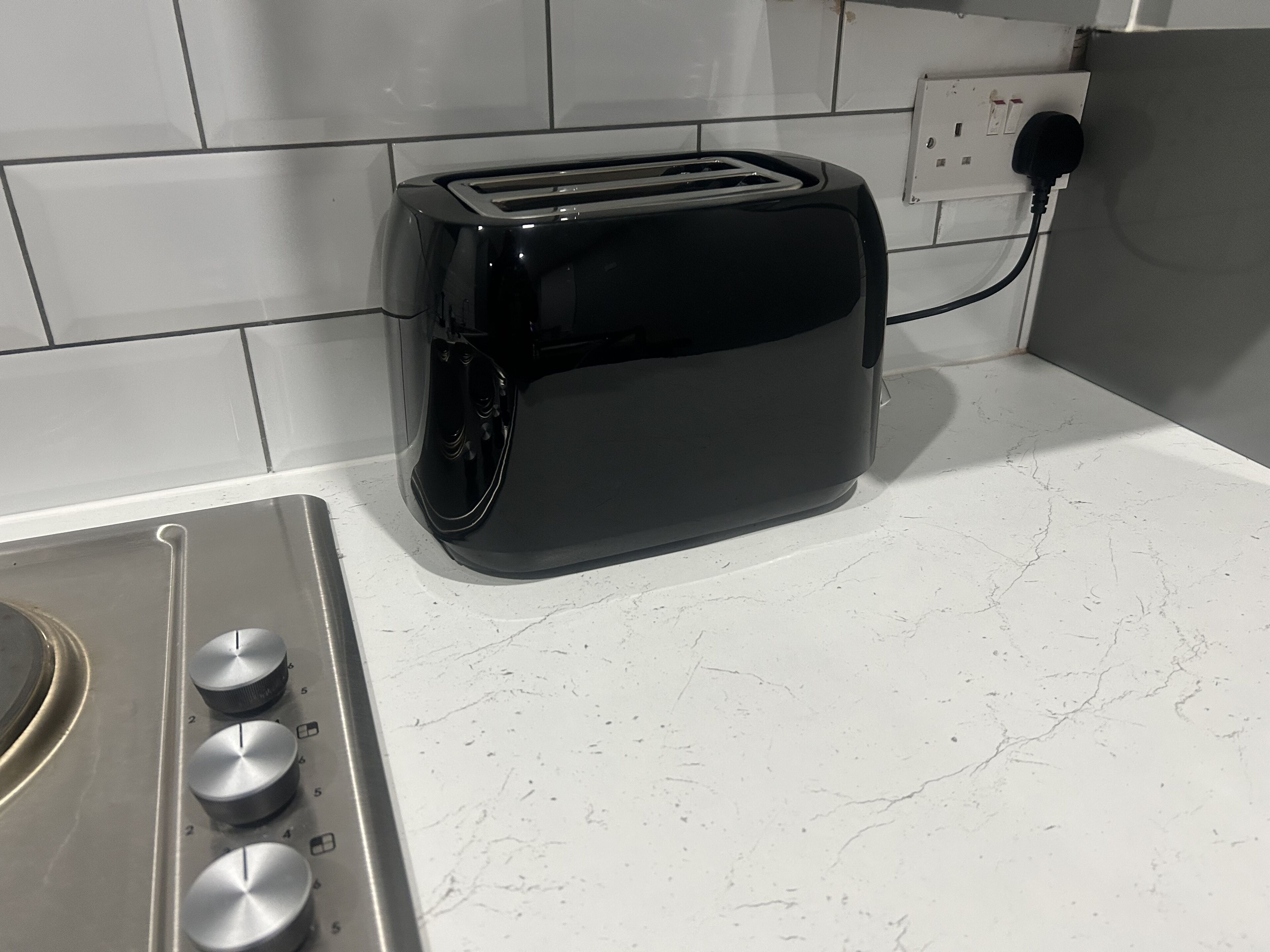 A kitchen with a black toaster on a white countertop, a stove with knobs, and a tiled backsplash.
