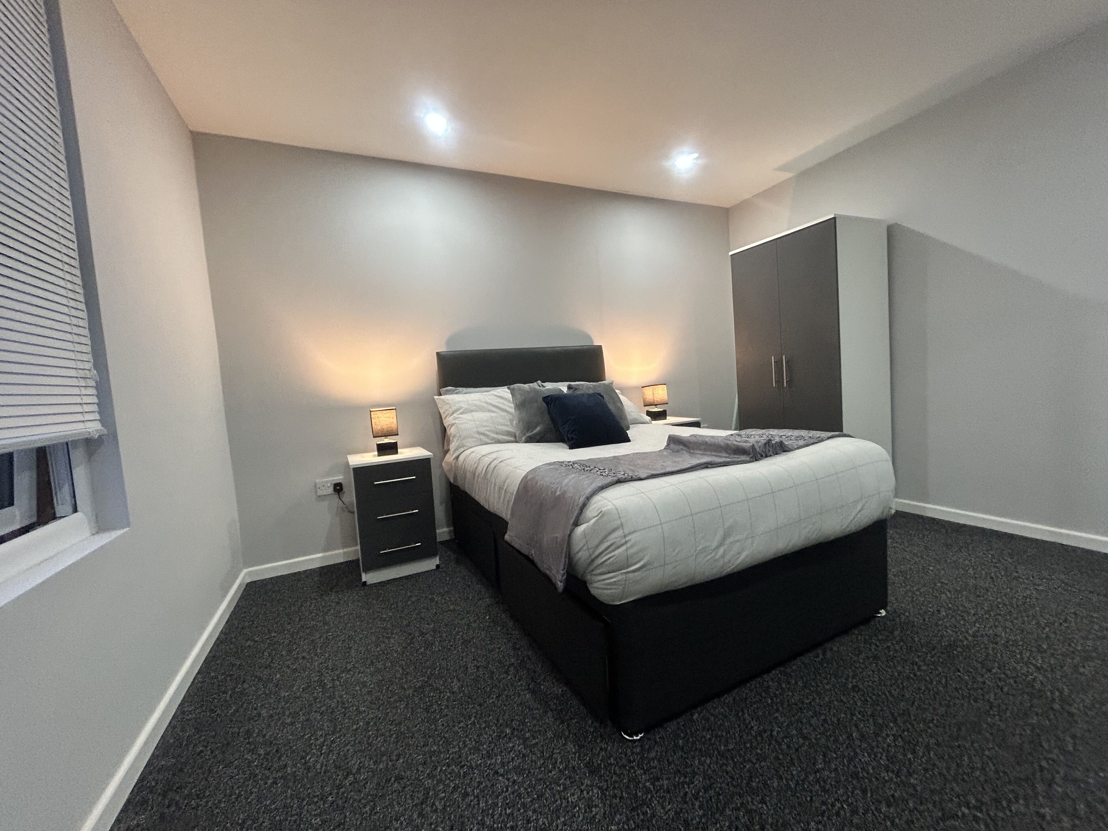 Une chambre à coucher moderne, avec un lit, des tables de chevet, une armoire et un sol recouvert d’une moquette.