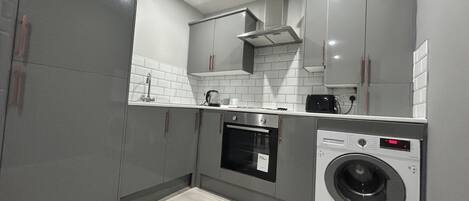 Una cocina compacta con armarios grises, horno integrado, lavadora y cafetera.