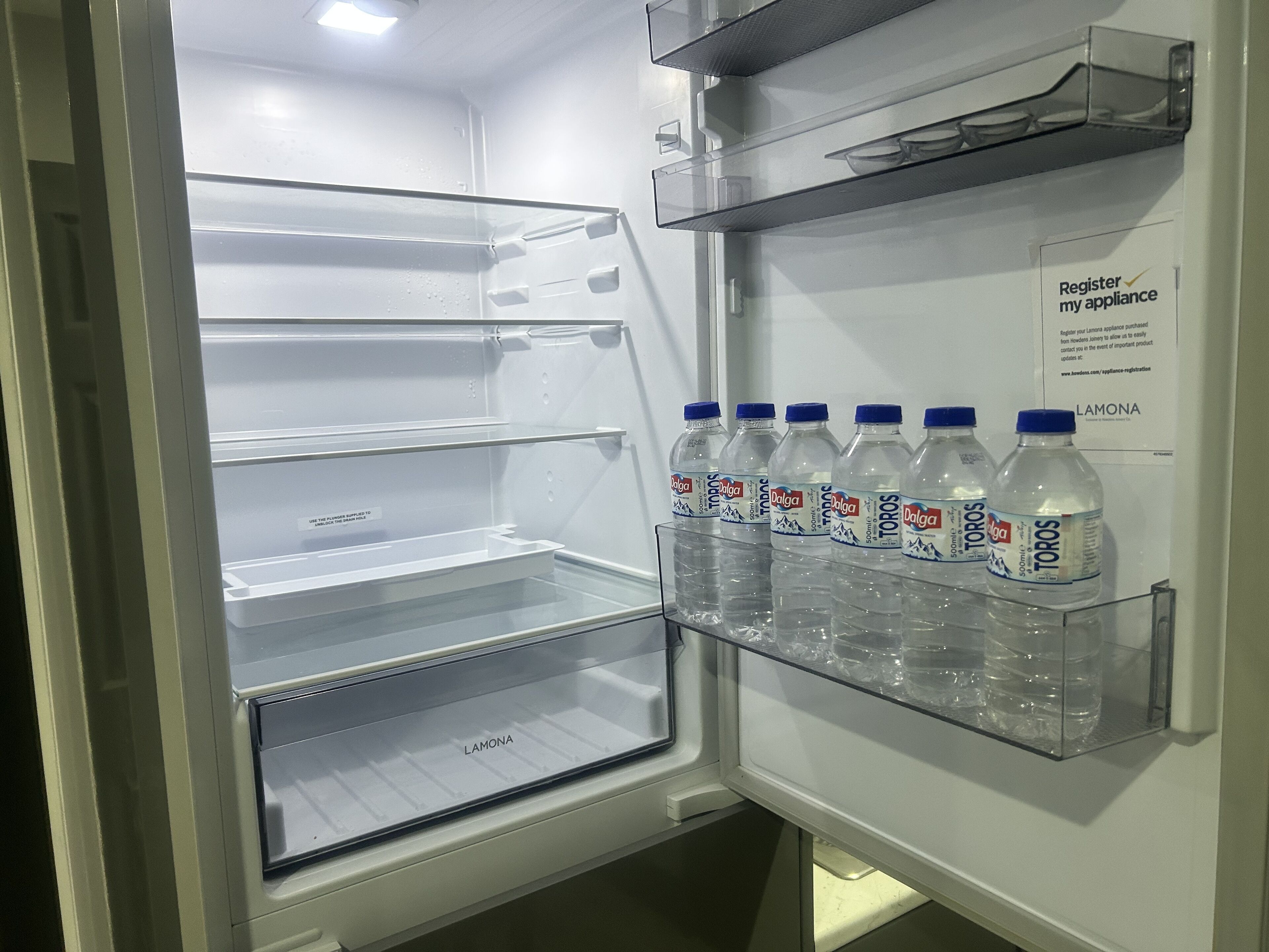 Ein leerer Kühlschrank mit einer Ablage für einen Wasserspender, auf der Wasserflaschen stehen.