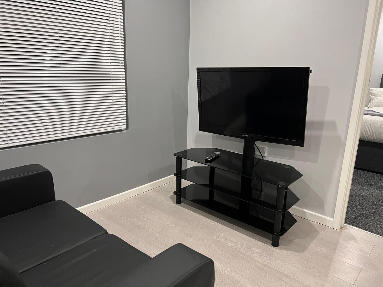 Una habitación moderna con una televisión de pantalla plana sobre un soporte negro, un control remoto y un sofá negro.