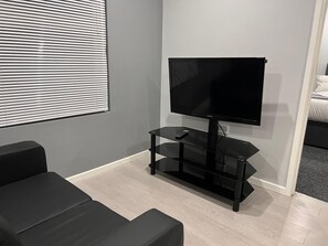 A modern room with a flat-screen TV on a black stand, a remote control, and a black sofa. - Private Luxury Apartment - Free Parking & Wi-fi (Coventry)