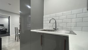 A modern kitchen with a stainless steel sink, white tiled backsplash, and grey cabinetry. - Private Luxury Apartment - Free Parking & Wi-fi (Coventry)