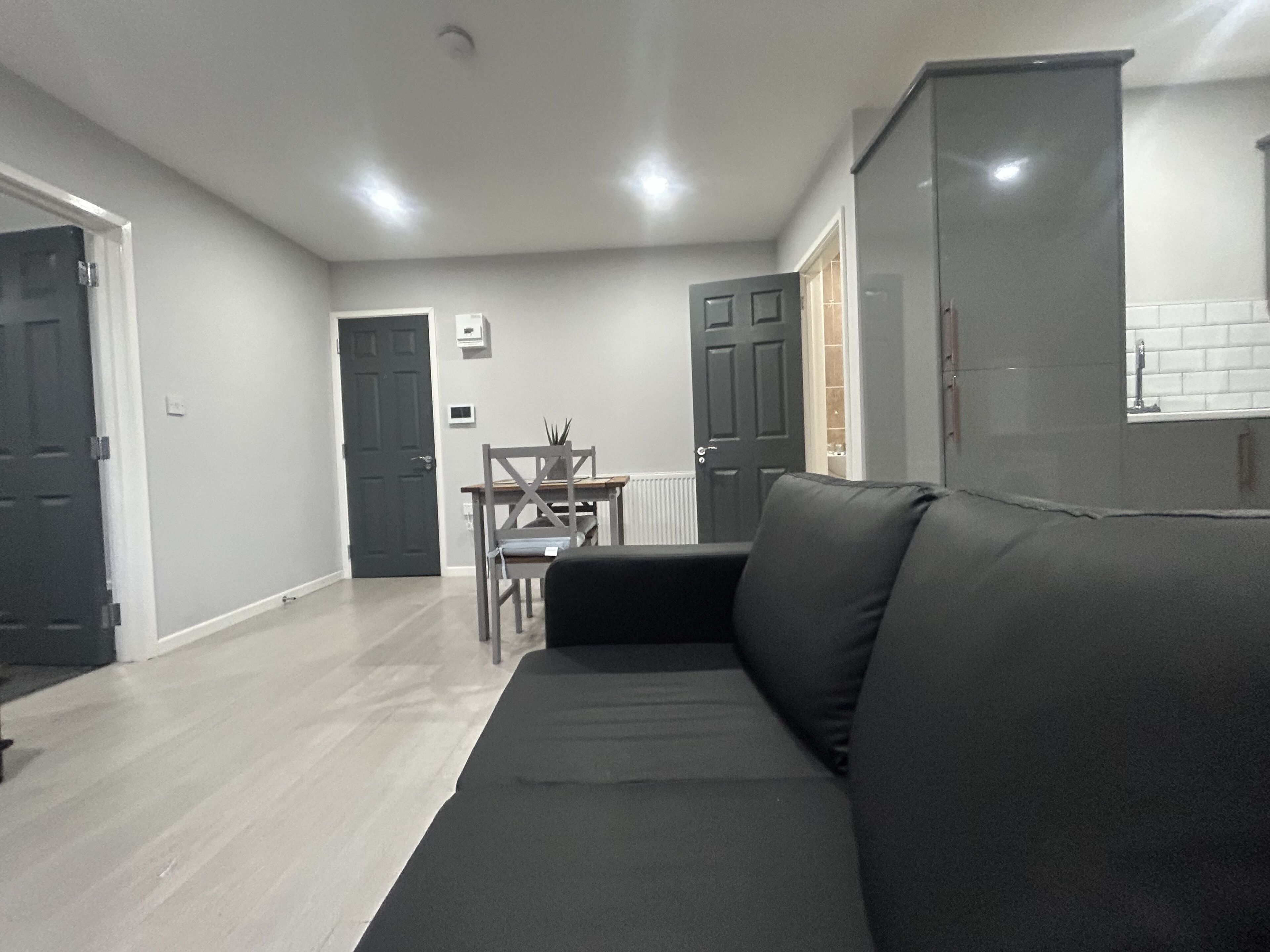 Una sala de estar moderna con un sofá negro, una mesa de comedor con sillas y una zona de cocina con armarios.