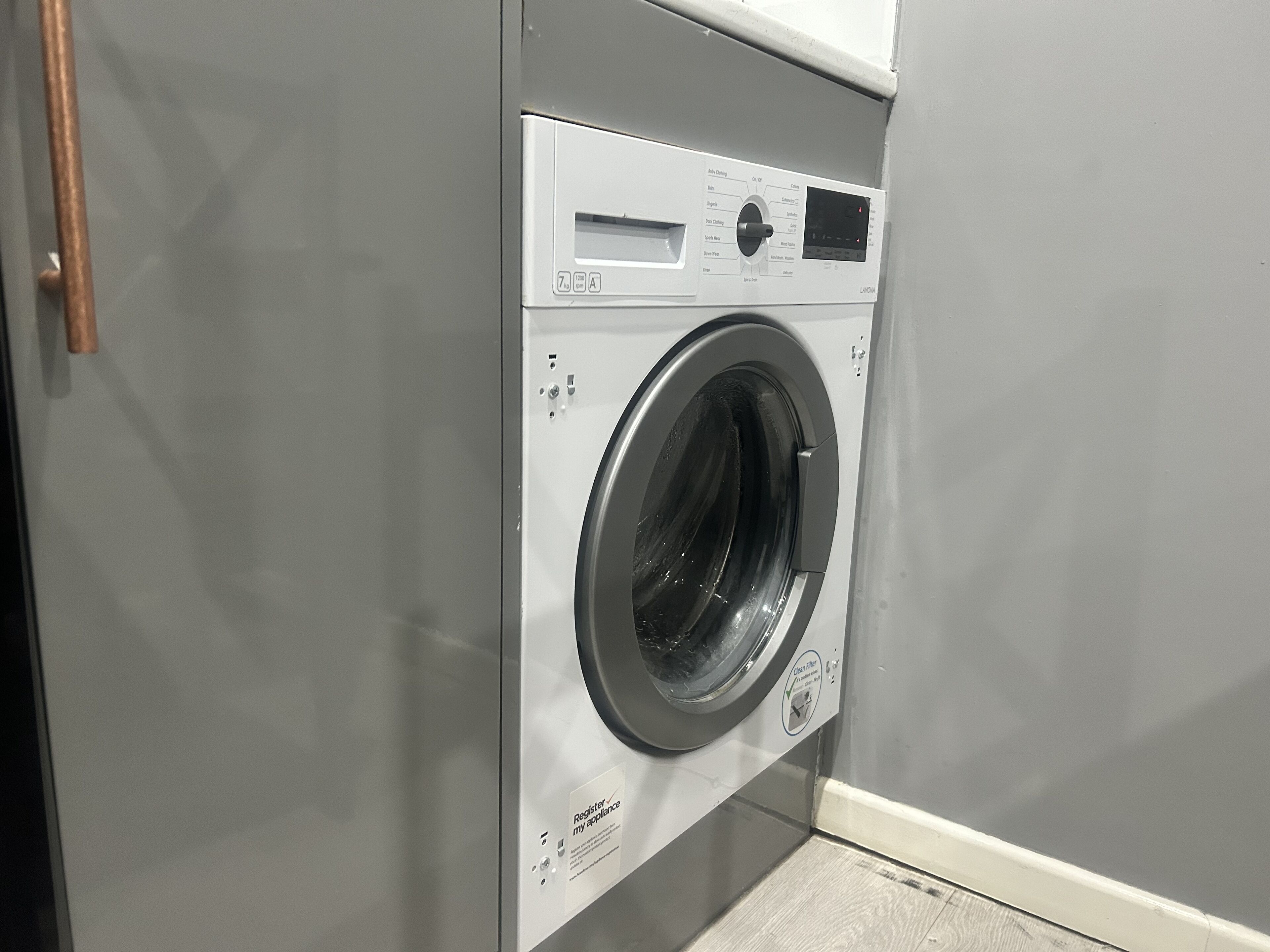A front-loading washing machine with a control panel, a door handle, and a label indicating it is a 'Laundry Room'.