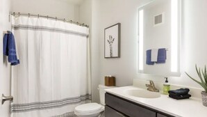Ein Badezimmer mit Duschvorhang, Toilette, Waschbecken, Spiegel und einem gerahmten Bild an der Wand.