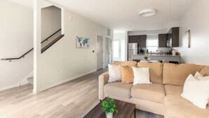 Ein modernes Wohnzimmer mit einem beigefarbenen Sofa, einem Couchtisch und einer Treppe, die in ein Obergeschoss führt.