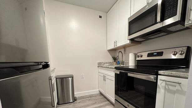 A modern kitchen with stainless steel appliances, white cabinetry, and a granite countertop.