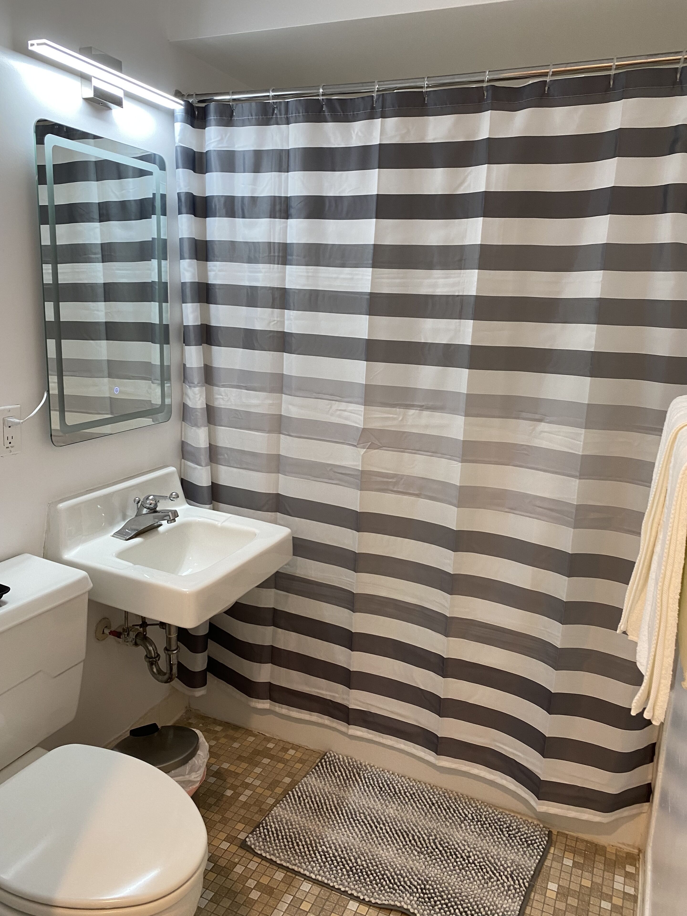 A bathroom with a striped shower curtain, a sink, a mirror, and a toilet.