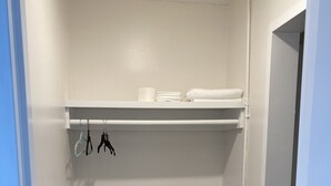 A small, white closet with a shelf and hanging space, carpeted floor, and a door leading to another room.