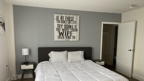 A bedroom with a bed, a nightstand, a wall-mounted lamp, and a door.