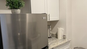 A modern kitchen with white cabinets, a stainless steel refrigerator, a granite countertop, and a small trash bin.