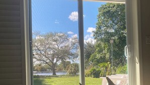 Une pièce avec vue sur un jardin arboré et une pelouse, accessible par une porte-fenêtre coulissante.