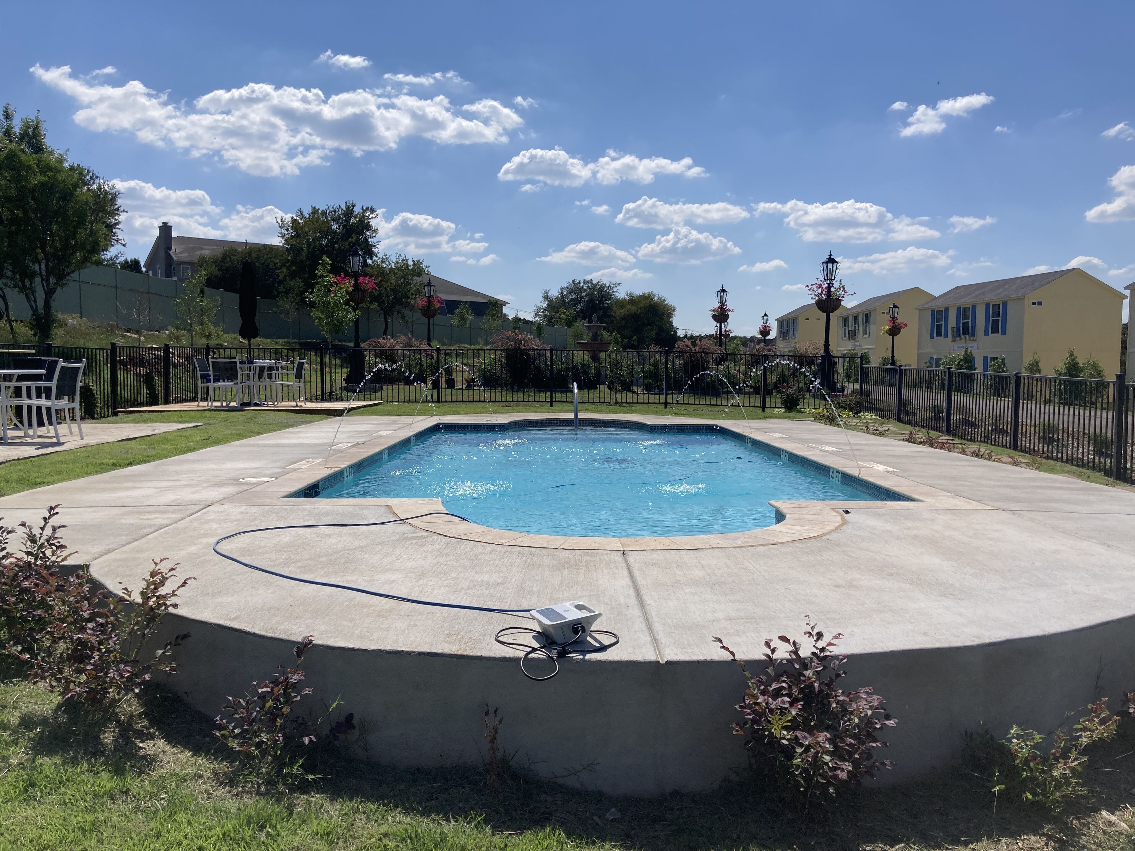 Une piscine rectangulaire entourée d’une terrasse en béton, équipée d’une pompe à eau et d’un câble d’alimentation.