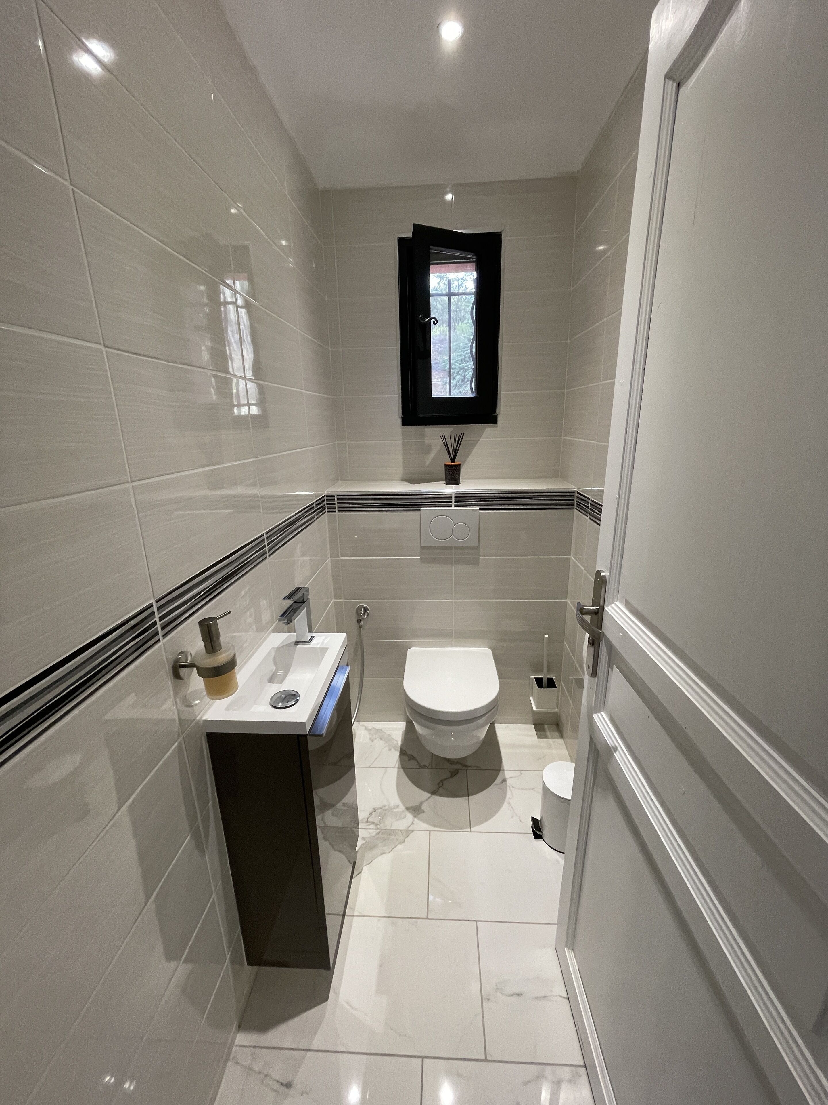 Un baño pequeño con inodoro, lavamanos y ventana sobre el lavamanos.