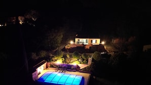 A nighttime view of a house with a swimming pool, surrounded by trees and a well-lit patio area. - Villa Provençale Avec Piscine (Le Cannet-des-Maures)