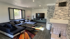A modern living room with a sectional sofa, a flat-screen TV, and a stone fireplace. - Villa Provençale Avec Piscine (Le Cannet-des-Maures)