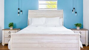 A bed with a wooden headboard, white bedding, and two bedside tables with potted plants.