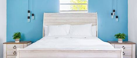 A bed with a wooden headboard, white bedding, and two bedside tables with potted plants.