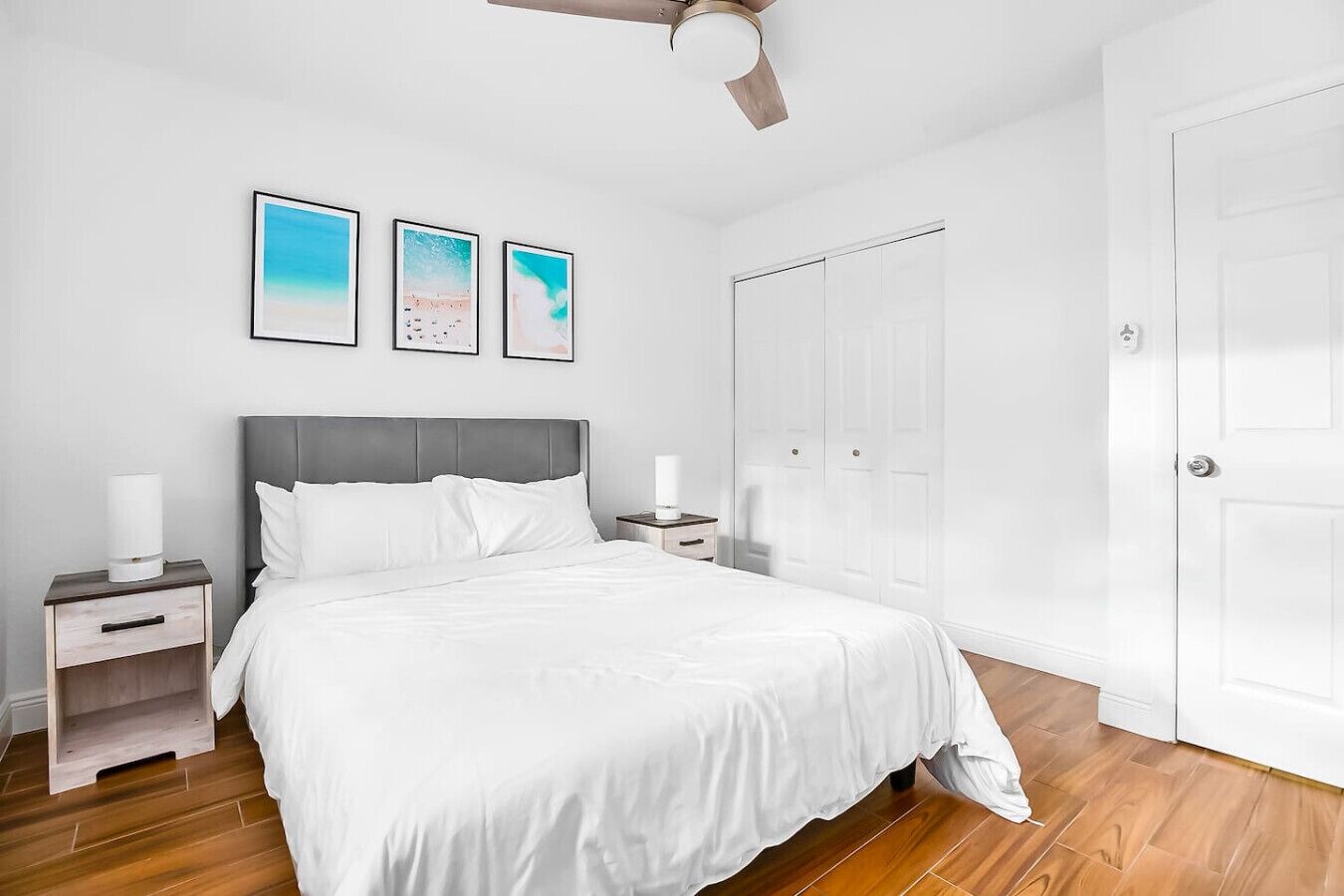A bedroom with a bed, nightstands, a ceiling fan, and a door.