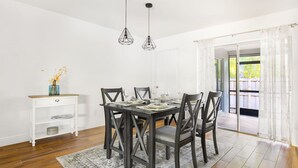 A dining area with a dark wooden table and chairs, a white console table with a vase, and a gray rug.