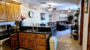 A kitchen with wooden cabinets, a black countertop, and a sink. There is a dining area with a table and chairs, and a living room with a couch and a coffee table. - Casa Blanca D 405 · Sandy Beach 2 BR Condo (Puerto Peñasco)