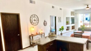 A kitchen with a marble countertop, wooden cabinets, a clock, and a dining area with a table and chairs.