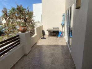 A balcony with a potted plant, a table with chairs, and a sliding glass door.
