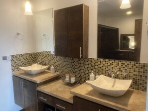 A bathroom with two vessel sinks, a mirror, and a tiled backsplash.