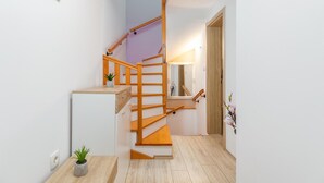 Una escalera de madera con barandilla, una mesita con una planta y un espejo en la pared.