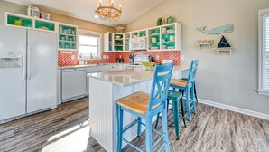 A kitchen with a central island, white cabinets, teal shelves, and blue chairs. - Wonder the Sea:Sweeping Intracoastal Views, Walk to Beach, Hot Tub, Pets Welcome (Surf City)