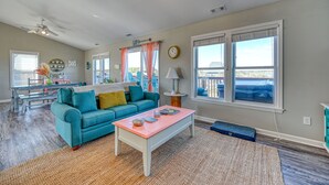A living room with a teal sofa, a pink coffee table, and a dining area with a table and chairs. - Wonder the Sea:Sweeping Intracoastal Views, Walk to Beach, Hot Tub, Pets Welcome (Surf City)