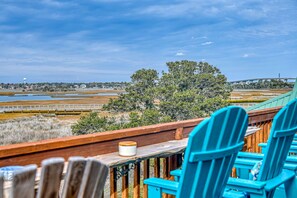 A wooden deck with blue chairs and a table, overlooking a coastal landscape with trees and a bridge. - Wonder the Sea:Sweeping Intracoastal Views, Walk to Beach, Hot Tub, Pets Welcome (Surf City)