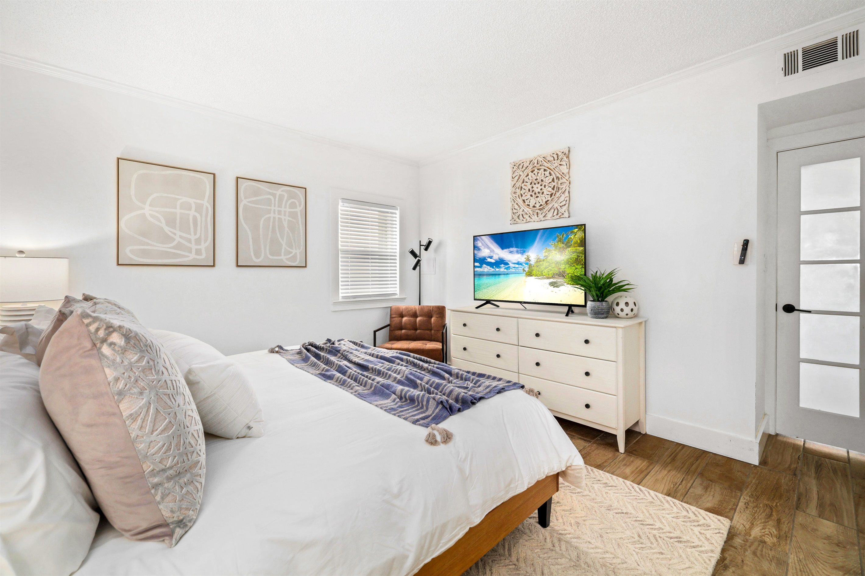 A bedroom with a bed, a TV, a dresser, and a door.