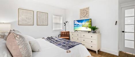 A bedroom with a bed, a TV, a dresser, and a door.