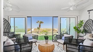 A modern outdoor seating area with wicker furniture, a woven coffee table, and a view of the beach. - Oceanfront Condo:1st Floor, Steps to the Ocean (Jacksonville Beach)