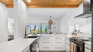A modern kitchen with white cabinetry, a large island, and a view to the outdoors. - Oceanfront Condo:1st Floor, Steps to the Ocean (Jacksonville Beach)