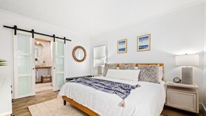 A bedroom with a bed, bedside tables, a lamp, and a wall-mounted mirror. - Oceanfront Condo:1st Floor, Steps to the Ocean (Jacksonville Beach)