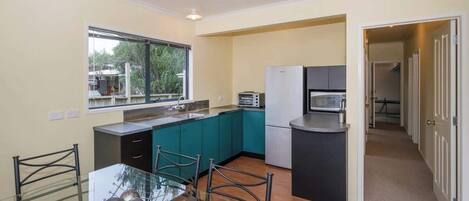 Una cocina compacta con armarios azul verdoso, un microondas y una mesa de vidrio con sillas.