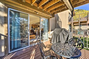 Une terrasse extérieure couverte, dotée d’une table et de chaises, une porte-fenêtre coulissante donnant sur une salle à manger intérieure, et une vue sur une colline.