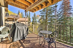 Une terrasse en bois dotée d’un barbecue couvert, de sièges d’extérieur et offrant une vue sur une montagne et des arbres.