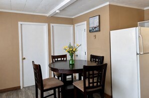 Uma sala de jantar com uma mesa redonda, quatro cadeiras, um vaso com flores amarelas e uma geladeira branca.