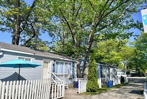 A row of mobile homes with a white picket fence, a blue umbrella, and a tree in the foreground.
