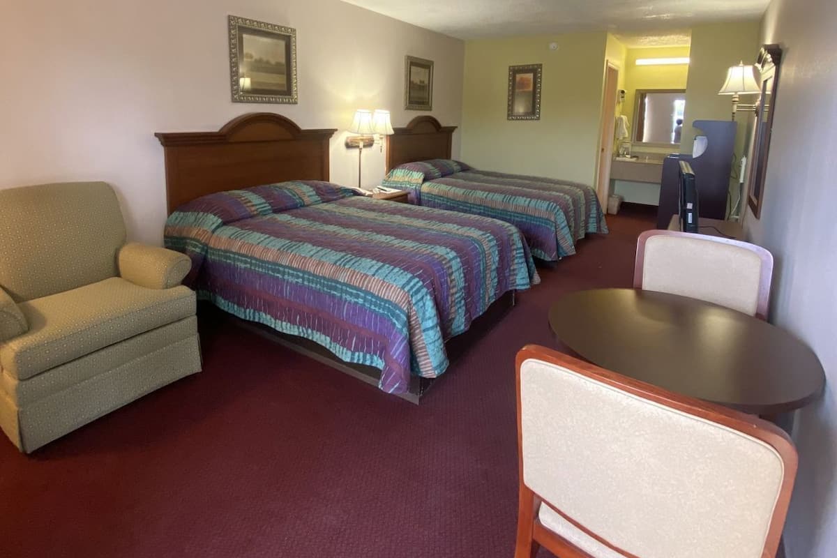 A hotel room with two beds, a chair, a small table, and a desk with a chair.