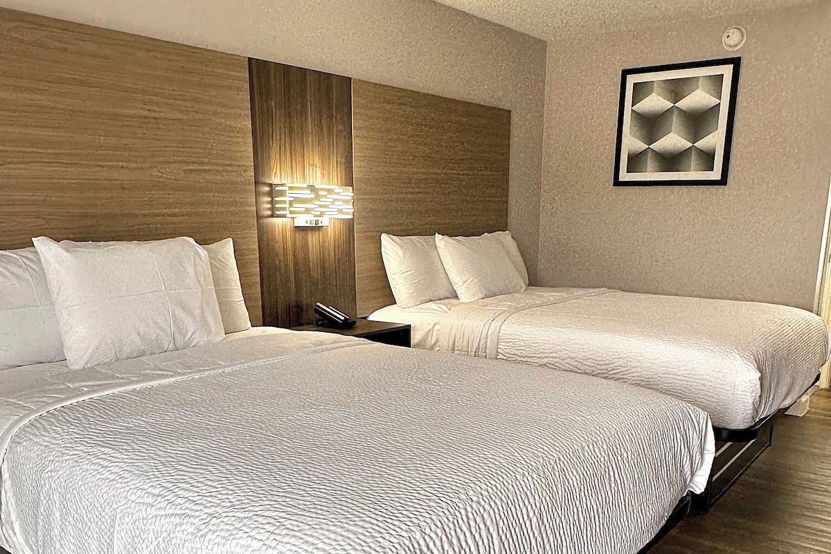 A hotel room with two beds, wooden headboard, wall-mounted light, and a framed artwork.