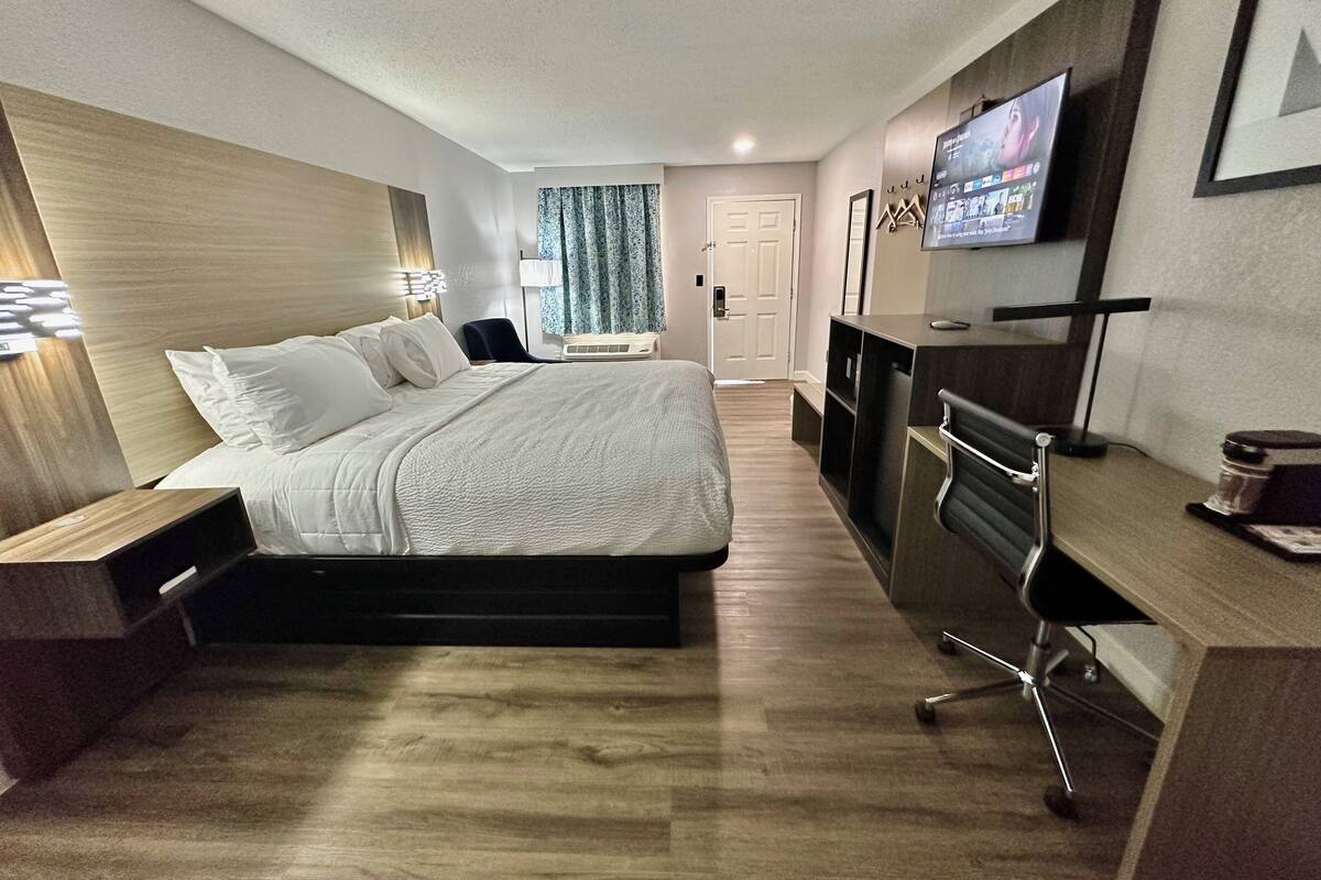 A modern hotel room with a large bed, a desk, a TV, and a door.