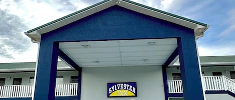 Un motel con fachada azul y blanca, un acceso cubierto y un cartel que dice 'Sylvester Inn'.