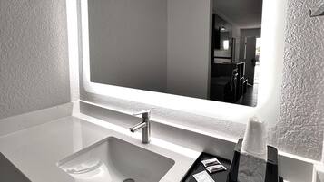 A modern bathroom with a large mirror, a sink, and a tissue dispenser.