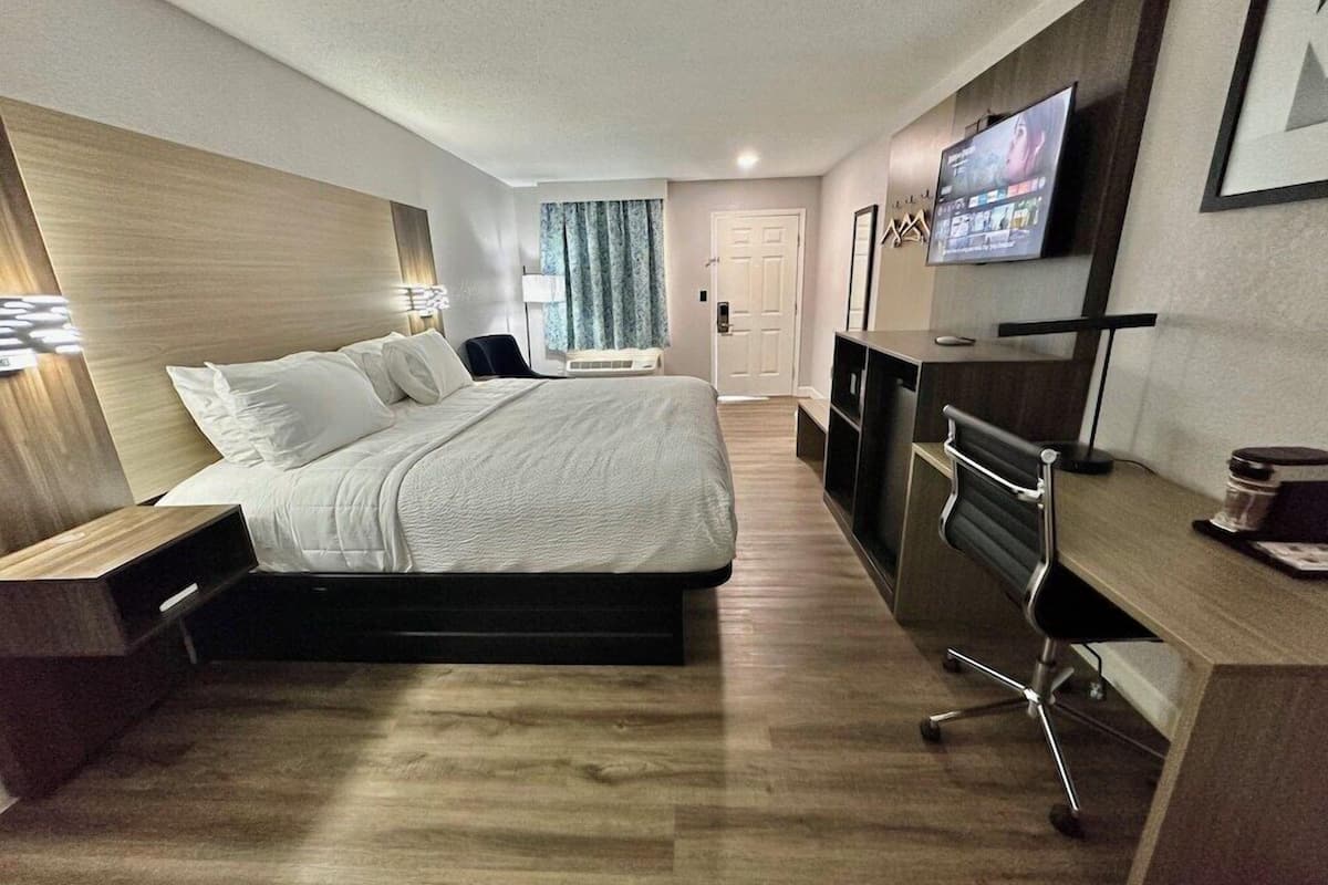 A modern hotel room with a large bed, a desk with a chair, a TV, and a door.